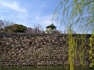 Osaka erken Bahar sırasında önünde mavi gökyüzü ve yeşil ağaç dalı ile kale duvarı ve kanal ile Japon Osaka Kalesi, Japonya