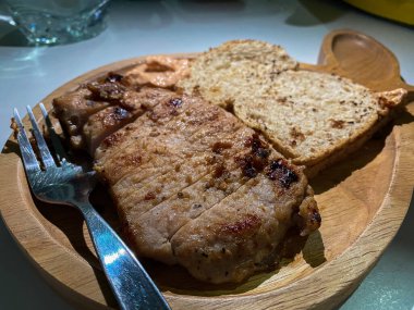 Domuz bifteği ve ızgara ekmek ahşap tabakta çatalla birlikte.