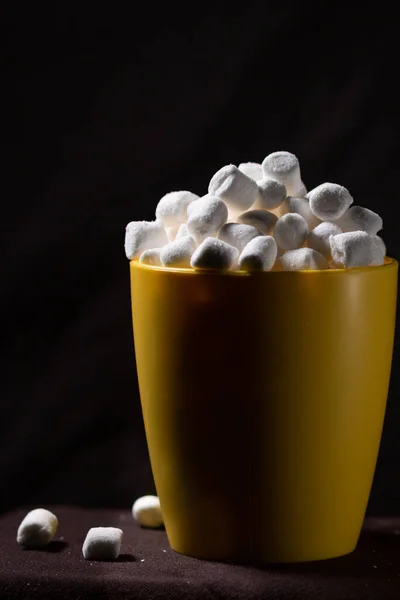 small marshmallows close up in a yellow cup, low key dark photography, empty space for text