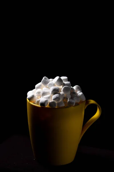 small marshmallows close up in a yellow cup, low key dark photography, empty space for text