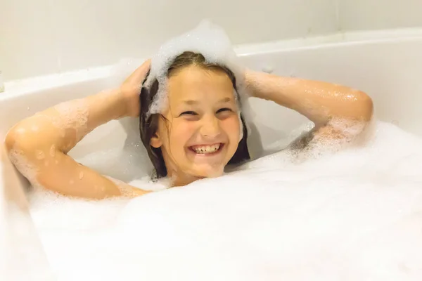幸せな子供は 彼女の頭を洗います 笑顔の子供の浴室で入浴します 小さな女の子は 石鹸とシャンプーの泡で頭を洗います 幸せな子供時代のコンセプト — ストック写真