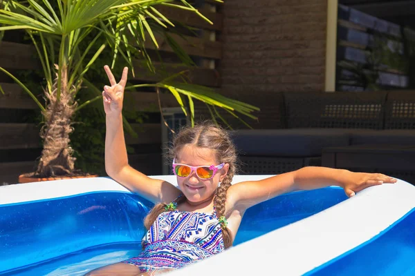小さな女の子は 水着とサングラスに身を包んだ 女の子は 裏庭の膨脹可能なプールの水で楽しんでいます 夏の日 幸せな子供時代 — ストック写真