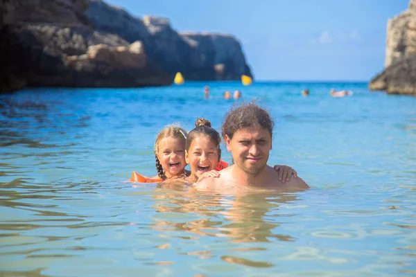快乐的家庭在海里游泳和玩耍 一个父亲和两个女儿在海滩上玩得很开心 爸爸和孩子们拥抱在一起 家庭度假的概念 海上假期 — 图库照片