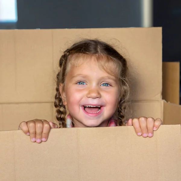 快乐的孩子有乐趣 喜欢玩捉迷藏 微笑的孩子从一个大纸板箱里往外看 转向一个新的家的概念 愉快的家庭搬迁 家庭打开包装 孩子玩盒子 — 图库照片