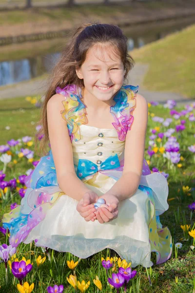 Adorable girl collects Easter chocolate eggs among flowers. — Stock Photo, Image