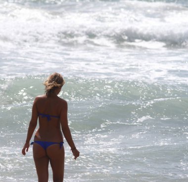 Güzel kız, arkadan, bikini ile gördüm su girer. Arka planda kaba deniz