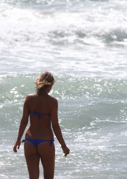 Beautiful girl, seen from behind, with bikini, who enters the water. Rough sea in the background