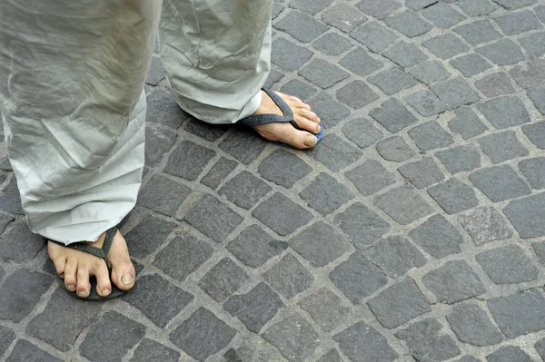 Dirty feet of a man wearing flip flops on the old stone floor. Bologna, Italy
