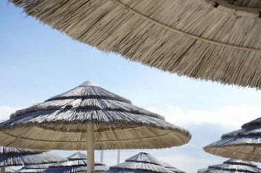 Mavi bir gökyüzü ve beyaz bulutlar üzerinde beyaz saman şemsiyeile güzel plaj tesisi. Plaj hayatı ve yaşam tarzı kavramı. Torre Lapillo, Salento, Apulia, İtalya