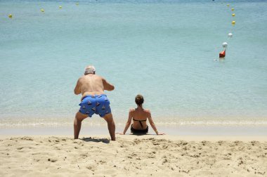 Komik ve komik bir durum. Yaşlı bir adam sahilde oturan güzel kız arka görünümü fotoğrafları çeker.