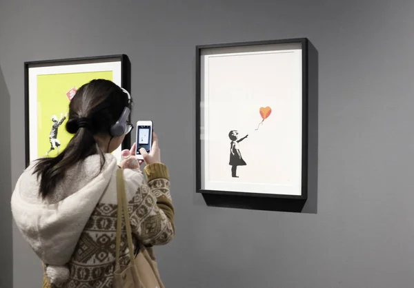 Ziyaretçiler, Banksy 'nin izinsiz sergisinde fotoğraf çekiyorlar. Balonlu kız..