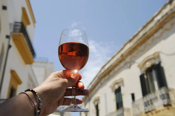 Glass of rose wine in man\'s hand against a blue sky background. Close-up. Relaxed mood concept in the historical italian city.