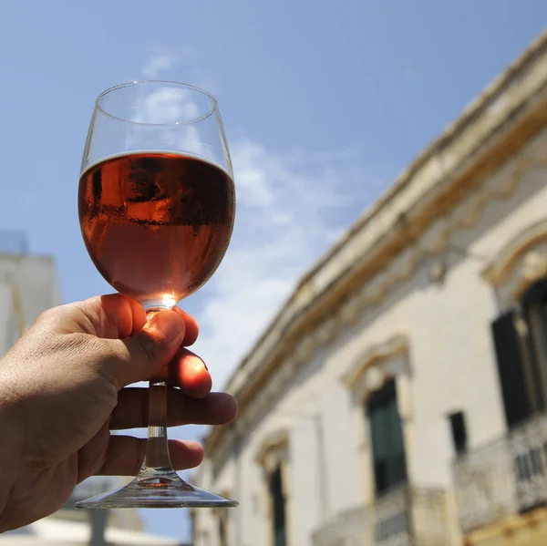 Glass of rose wine in man\'s hand against a blue sky background. Close-up. Relaxed mood concept in the historical italian city.