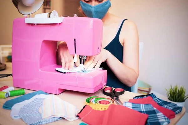 Dikiş makinesiyle çalışan kadın Coronavirus 'un yayılmasını önlemek ve durdurmak için moda yüz maskesi yapıyor - ev yapımı üretim konsepti - kullanılmış kıyafetlerin yeniden kullanımı - ana odak noktası eller
