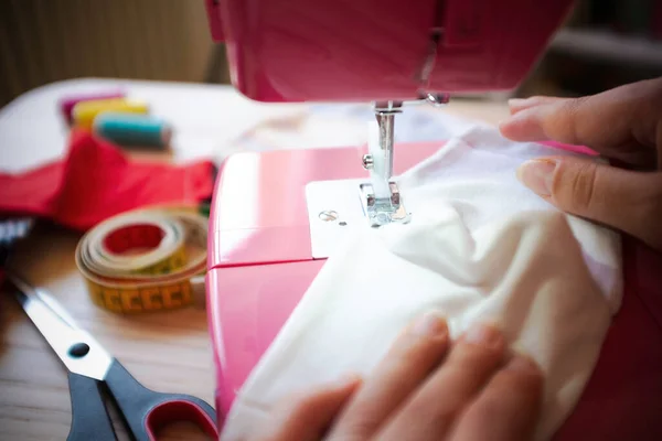 Kadın ellerinin, dikiş makinesiyle yüz maskesi yaparak Coronavirus 'un yayılmasını önlemesi ve durdurması - ev yapımı üretim konsepti - kullanılmış kıyafetlerin yeniden kullanımı - ellere odaklanma