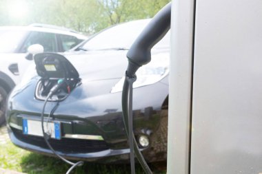 Elektrik kablosu olan şarj istasyonunda güneş ışığı arka planında bulanık doğaya bağlı EV Car veya Electric Car. Çevre dostu alternatif enerji kavramı
