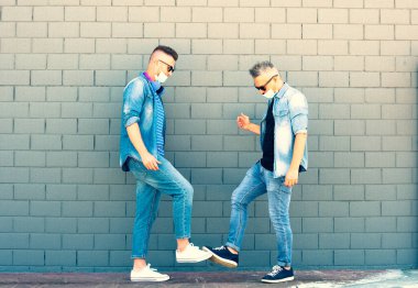 Coronavirüs salgınından sonra iki arkadaş ayaklarıyla yeni sosyal mesafeli selamlaşmalar yapıyor - koruyucu maskeleri indirmiş adamlar - yeni normal kavram içinde fiziksel mesafe ve güvenlik selamlaması kavramı