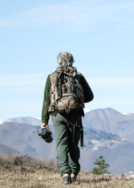 Hiker senior man with backpack and camera walking on the mountain path - Active traveler pensioner with grey hair  - Discovery travel destination concept, Motivation - Rear view with copy space clipart