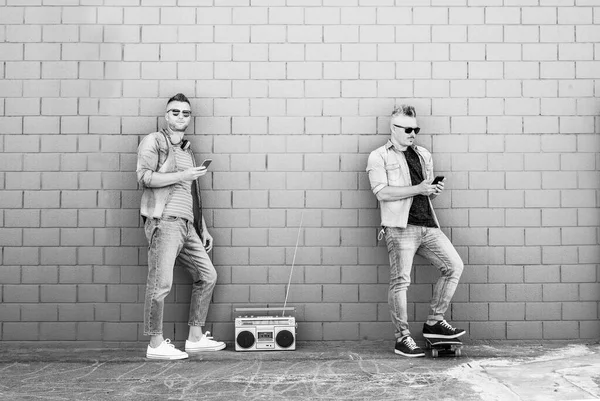 Dwóch Młodych Ludzi Patrząc Telefon Komórkowy Oprzeć Się Ścianę Cegły — Zdjęcie stockowe