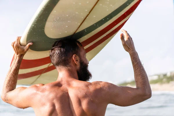 Kafasında sörf tahtası olan genç hippi bir jestle dostlarını selamlıyor - ekstrem sporlar yaparak eğlenen adam - denizdeki sörf tahtasıyla spor yapan sakallı adam - yaşam tarzı, özgürlük konsepti