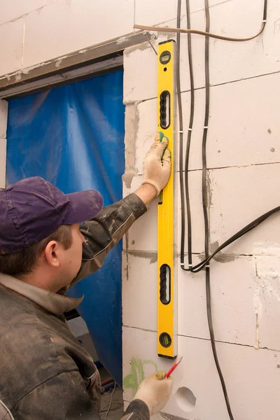 The Builder checks the level of the wall at the construction site