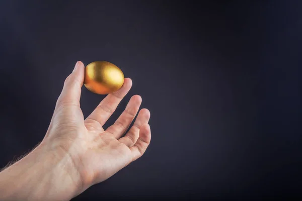 Ο άνθρωπος χέρι που κρατά το χρυσό αυγό σε μαύρο φόντο — Φωτογραφία Αρχείου