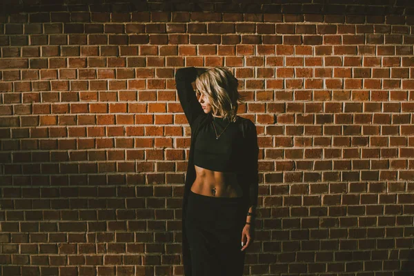 Deldi göbek kırpma üst bekleyen bir tuğla duvara kafa, eller gün batımında giymiş sarışın kadınla
