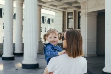 Genç Anne kızı kucağında taşıyan şehir etrafında bir yürüyüş sırasında sıcak güneşli bir günde