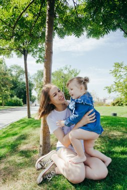 Genç bir anne ve 3 yaşında kızı sıcak güneşli bir günde bir şehir parkı ağacında altında oynamak portre