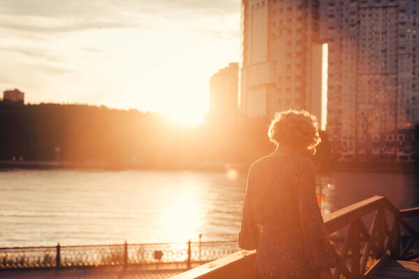 Woman walking on a wooden stairs near river bank in an urban landscape park at the sunset, looking to the side