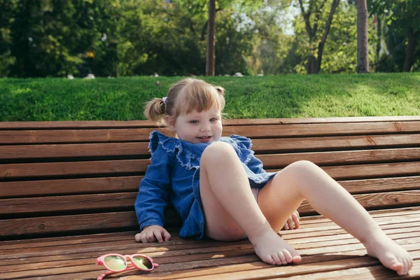 Küçük kız sıcak güneşli bir günde bir şehir parkta bankta oturmuş