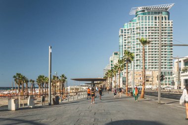 Tel Aviv / İsrail-13 / 10 / 18: güneşli bir yaz gününde Tel Aviv 'de gezinti alanında yürüyen insanlar; Royal Beach Hotel sağ tarafta.