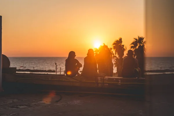 İnsanlar sıcak bir yaz akşamında Tel Aviv 'deki gezinti güvertesinde Akdeniz' de gün batımını seyrediyorlar.