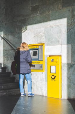 Bamberg / Almanya-2 / 1 / 19: Alman kasabasındaki bir caddedeki Deutsche Postbank ATM 'sinden para çeken bir kadının dikiz görüntüsü. Postbank, Deutsche Bank 'ın perakende bankacılık bölümüdür.