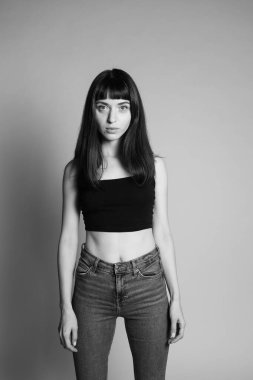 Siyah yelekli güzel bir esmer kadının stüdyo portresi, sandalyenin arkasında duruyor, elleri çapraz, ciddi ciddi kameraya bakıyor, düz gri bir arka plan üzerinde