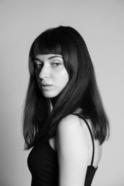 Siyah spagetti askılı güzel esmer bir kadının stüdyo portresi, ciddi ciddi yana bakıyor, düz gri bir arka plan karşı yarı dönmüş