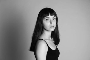 Siyah spagetti askılı güzel esmer bir kadının stüdyo portresi, ciddi ciddi kameraya bakıyor, yarım yamalak gri bir arka plana bakıyor.