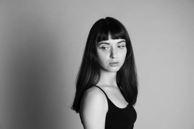 Siyah spagetti askılı güzel esmer bir kadının stüdyo portresi, ciddi ciddi yana bakıyor, düz gri bir arka plan karşı yarı dönmüş