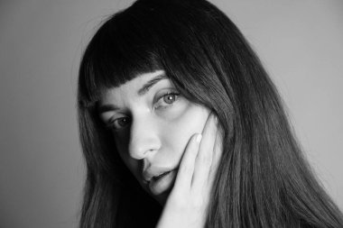 Güzel esmer bir kadının stüdyo portresini kapat, el yanağında, kameraya bakıyor, yarı dönüş, düz gri bir arka plan