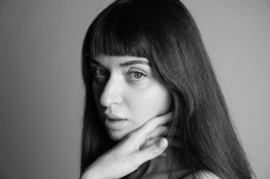 Güzel esmer bir kadının stüdyo portresini kapat, el yanağında, kameraya bakıyor, yarı dönüş, düz gri bir arka plan