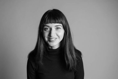 Güzel esmer bir kadının stüdyo portresini kapat, katlanmış siyah polo yaka kazak giyen, kameraya bakan, düz gri bir arka plan