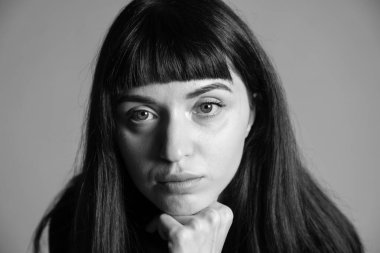 Güzel esmer bir kadının stüdyo portresini kapat, el çenesinde, ciddi ciddi kameraya bakıyor, düz gri bir arka planda.