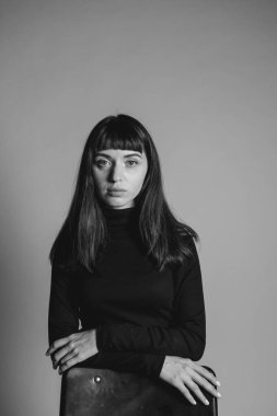 Güzel esmer bir kadının stüdyo portresini kapat. Kollarını kavuşturup sandalyenin arkasında duruyor. Gerçekten kameraya bakıyor.