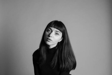 Güzel esmer bir kadının stüdyo portresini kapat, kameraya bak, düz gri bir arka planda.