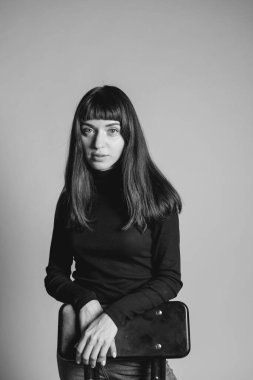 Güzel esmer bir kadının stüdyo portresini kapat, katlanmış siyah polo yaka kazak giyiyor, gülümsüyor, kameraya bakıyor, düz gri bir arka plana bakıyor.