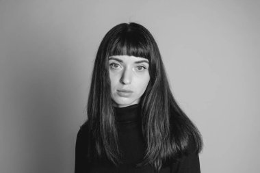 Güzel esmer bir kadının stüdyo portresini kapat, kameraya bak, düz gri bir arka planda.