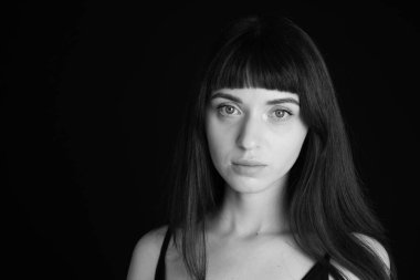 Siyah spagetti askılı güzel esmer bir kadının stüdyo portresi, düz siyah bir arka planda, kameraya bakıyor.