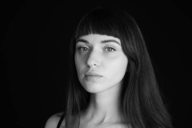 Siyah spagetti askılı güzel esmer bir kadının stüdyo portresini kapat, kameraya bak, düz siyah bir arkaplanda.