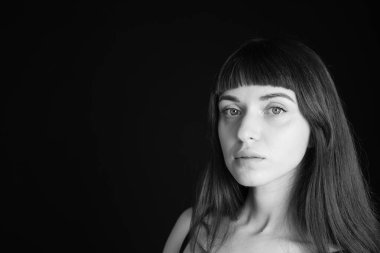 Siyah spagetti askılı güzel esmer bir kadının stüdyo portresi, düz siyah bir arka planda, kameraya bakıyor.