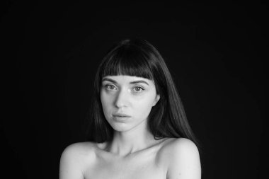 Güzel esmer bir kadının stüdyo portresi, düz siyah bir arka planda, kameraya bakıyor.